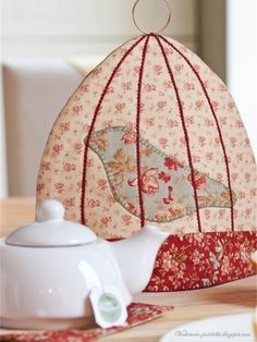 a tea pot with an umbrella shaped like a birdcage hanging from it's side