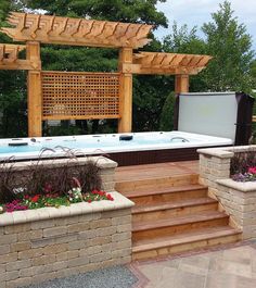 a hot tub sitting next to a wooden pergolated structure with flowers in the foreground