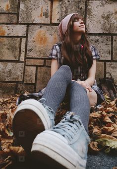 a young woman sitting on the ground with her feet up in front of a brick wall