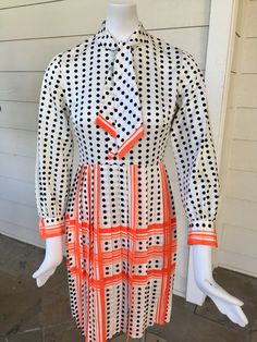 "Unique 70s fit and flare style dress. White background with black polka dots. Skirt and cuffs are accented in a bright orange checkered plaid type design. Darts on the front. Skirt has been permanently pleated. Neck is high collared with a tied scarf. Cuff button is gold with an anchor design. Back has a hook and thread closure and a 14\" zipper Dress in in excellent vintage condition, no signs of wear or stains. No name brand, size or fabric tags. Possibly material is a nylon, polyester or Dac Retro Polka Dot Workwear Dresses, Retro Polka Dot Dress For Work, Retro Polka Dot Lined Dresses, Retro Polka Dot Dress For Daywear, Retro Polka Dot Day Dresses, White Retro Dress For Fall, Orange Retro Dress For Workwear, Dress White Background, Polka Dots Skirt