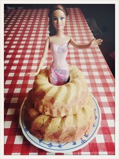 a barbie doll is sitting on top of a bundt cake that has been placed on a checkered tablecloth