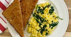 two pieces of toast on a plate with eggs and spinach next to each other