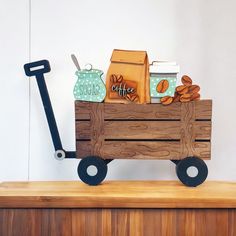 a wooden wagon filled with assorted items sitting on top of a wooden table next to a white wall