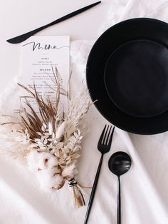 a table setting with black plates and utensils, napkins, and menu