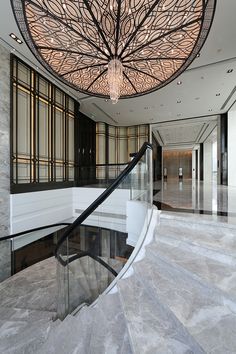 an elegant staircase with glass railings and chandelier in a building's lobby