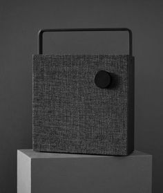 a black speaker sitting on top of a white block in front of a gray wall