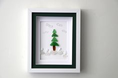 a white frame holding a green and white paper cutout with a pine tree in the middle