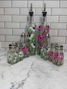 four glass bottles with painted flowers on them sitting on a marble counter next to a tile wall