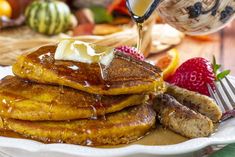 stack of pancakes with syrup and butter on white plate next to strawberries, oranges and other fruit