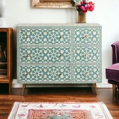 a blue and white dresser sitting next to a purple chair in a room with a painting on the wall