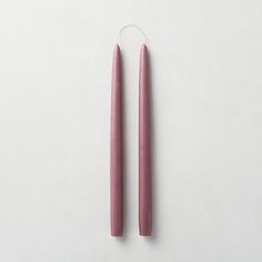 two pink candles sitting next to each other on a white surface with one candle in the middle