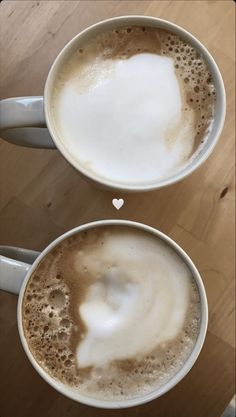 two white cups filled with liquid on top of a wooden table