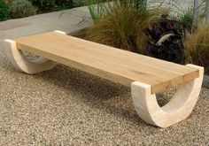 a wooden bench sitting on top of a gravel covered ground next to tall grass and plants