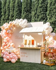 an outdoor bar is decorated with pink balloons and white furniture, along with greenery