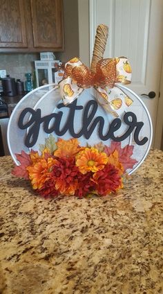 a sign that says gather on top of a granite countertop with fall leaves and flowers