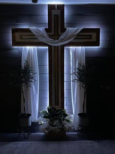 the cross is lit up with flowers and greenery in front of white drapes