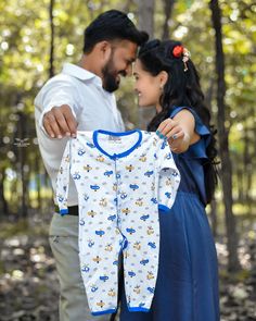 a man and woman are holding up a baby's pajamas in the woods while they look at each other