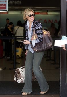 a woman is walking out of an airport with her handbag and purse in tow