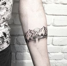 a man's arm with a mountain and lake tattoo on the left inner forearm