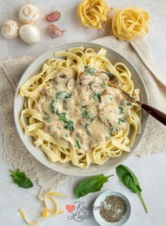 a bowl of pasta with sauce and spinach on the side next to two garlic cloves