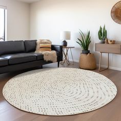 a living room with a black leather couch and white round rug on the hardwood floor