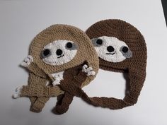 two crocheted hats with slotty faces on them, one is brown and the other is white