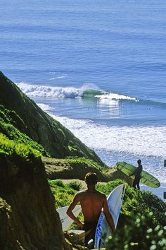 two surfers are walking up the hill to the beach with their surfboards in hand