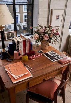 a wooden desk topped with books next to a window filled with flowers and other items