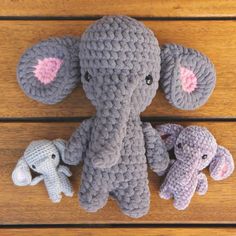 three crocheted elephants sitting next to each other on a wooden surface with one elephant holding the baby's ear