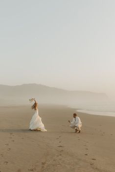 a man kneeling down next to a woman on top of a sandy beach