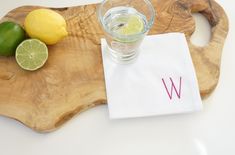 a wooden cutting board topped with a glass of water next to lemons and limes