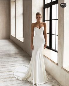 a woman in a white wedding dress standing next to a window