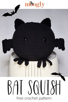 a crocheted bat stuffed animal sitting on top of a white vase with bats flying around