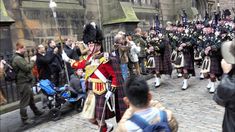 a group of men in kilts marching down a street with people watching them from the sidelines