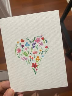 a person holding up a card with watercolor flowers in the shape of a heart