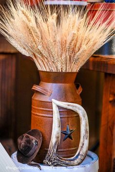 a vase with some dried plants in it and a cowboy hat on the table next to it