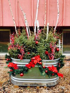 two metal planters filled with red and green christmas decorations sitting in front of a building