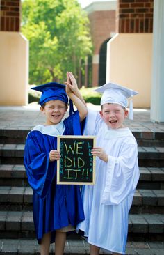 two children in graduation gowns holding up a sign