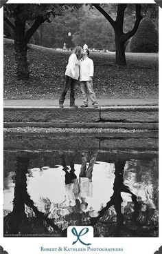 two people standing next to each other in front of water with trees and grass behind them