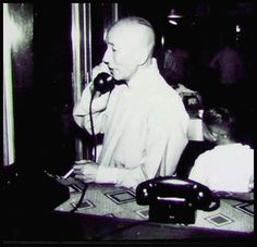 an old black and white photo of a man sitting at a desk talking on the phone