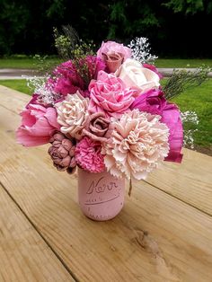 a pink vase filled with lots of flowers sitting on top of a wooden table next to grass