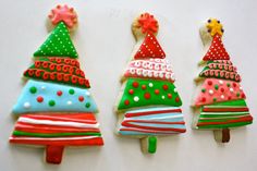 three decorated christmas trees sitting on top of a white table next to each other with red, green, and blue frosting