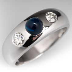 This fabulous vintage ring is centered with a flush set, round sapphire cabochon with a high dome, weighing 1.10 carats. The sapphire is flanked on either side by a flush set, round transitional brilliant cut diamond. The ring measures 7.6mm at the top, rises 6.5mm above the finger, tapering to 4.2mm wide and 1.4mm thick at the base of the shank. It is currently a size 8.5. The ring has light porosity. Timeless Cabochon Sapphire Ring, Classic Cabochon Sapphire Ring For Formal Occasions, Classic Formal Cabochon Sapphire Ring, Classic Formal Sapphire Cabochon Ring, Formal Fine Jewelry Domed Cabochons, Formal Domed Cabochons Fine Jewelry, Classic White Gold Sapphire Cabochon Ring, Timeless Round Cabochon Sapphire Ring, Classic White Gold Cabochons For Anniversary