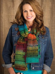 a woman standing in front of a wooden wall wearing a denim jacket and colorful scarf