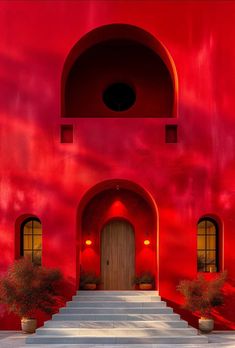 a red building with steps leading up to the door and two potted plants on either side