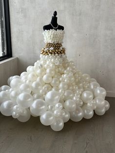 a dress made out of balloons in front of a window with a mannequin on top