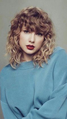 a woman with curly hair wearing a blue sweater and red lipstick is posing for the camera