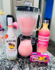 a blender filled with pink lemonade next to two bottles of juice and some candy