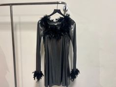 a black dress with feathers hanging on a hanger in front of a white wall