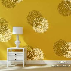 a white table sitting next to a yellow wall with flowers on it and a lamp